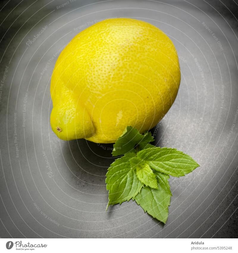 One lemon and mint leaves on a black plate Lemon Mint Yellow Green whole lemon citrus fruit Lemonade Sour Acid Fresh Summer Refreshment Plate Black