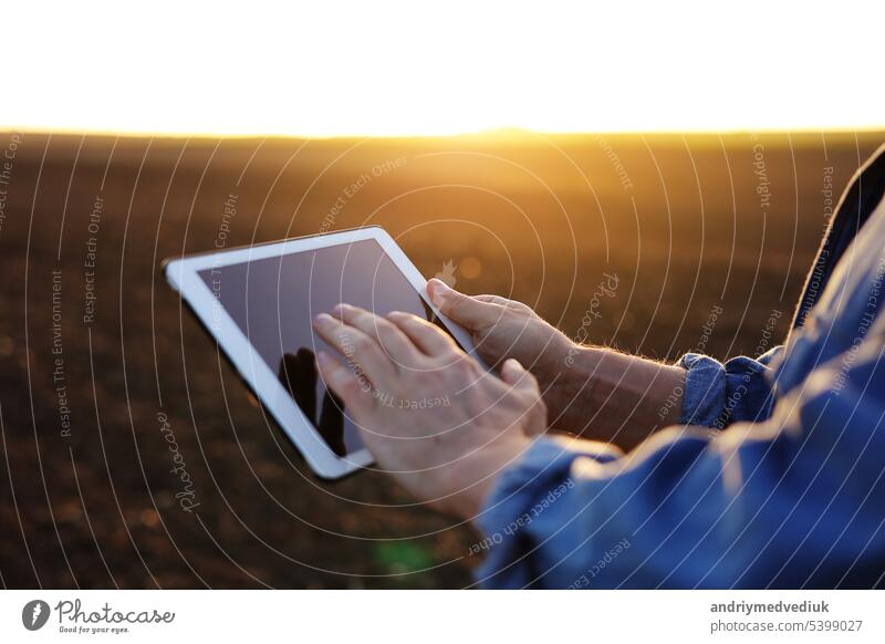 Cropped shot of male farmer's hands use digital tablet on plowed field for control of soil quality, land readiness for sowing crops and planting vegetables. Smart farming technology and agriculture