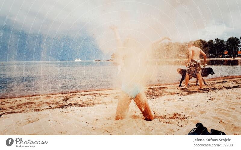 Girl kneeling in the sand on the beach. Throws the sand in the air. Behind a boy with a black dog running into the water. Summer vacation holidays Beach