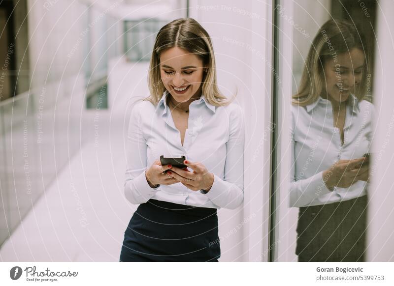 Young business woman using mobile phone in the office hallway caucasian professional businesswoman female people person confident talking cellphone