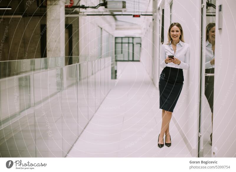 Young business woman using mobile phone in the office hallway caucasian professional businesswoman female people person confident talking cellphone