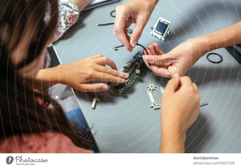 Female teacher helping girl student to assemble electrical circuit in a robotics class unrecognizable female explaining child electronic connect teaching