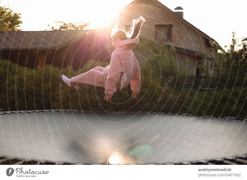 Happy little child girl having fun and jumps on trampoline outdoors, at backyard of the house on sunny summer day, active recreation on summertime vacation. Happy childhood concept. Children's day.