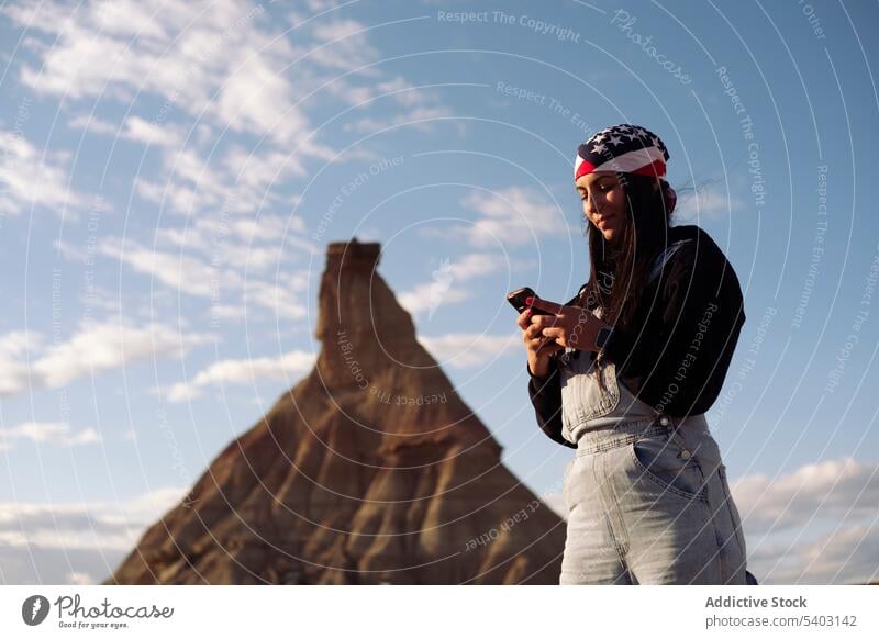 Young woman browsing smartphone beside hill under blue sky tourist traveler vacation tourism young female trip spain sandstone device journey casual explore