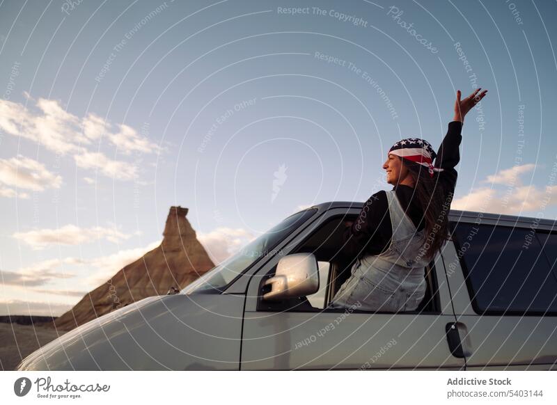 Young woman sitting on window by driver seat while admiring dessert usa flag admire tourist traveler hill vacation tourism smile nature blue sky happy young