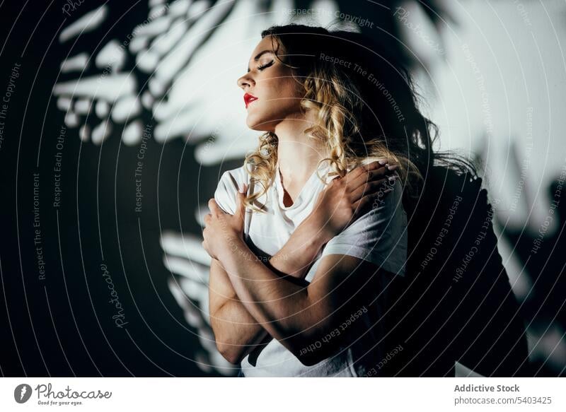 Young woman with red lips standing near wall sensual eyes closed shadow reflection posture female young shirt allure style sunlight feminine sensitive calm