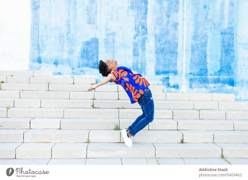 Young man jumping back flip on street stairs leap energy urban wall city parkour male young perform athlete black african american blue ethnic above ground