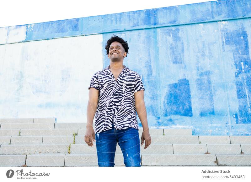 Young black man standing on street stairs energy urban smile wall city male young perform gaze african american blue glance joy ethnic sincere appearance