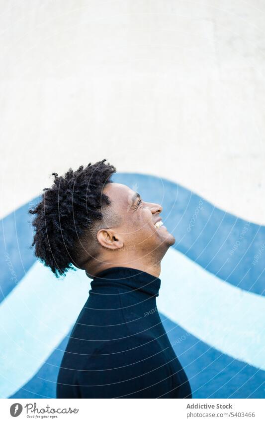 Cheerful young man with curly hair and head lifted up positive trendy hairstyle happy smile looking up individuality male african american calm afro appearance