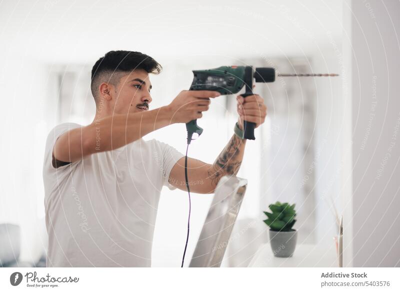 Side view of serious man drilling the wall on a ladder apartment build builder electric engineer handyman hole repair home housework improvement indoor