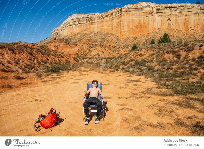 Teenage boy sitting on folding chair in desert suntan trip tourist sunbath fabric chair sunglasses traveler teen canyon teenager mountain rojo teruel rock