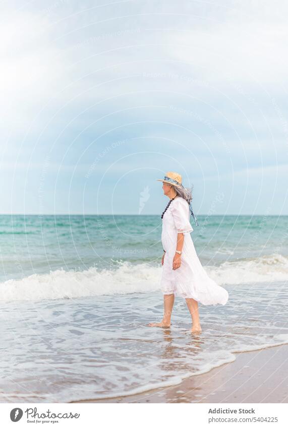 Serious woman walking on sandy beach freedom enjoy vacation summer sea nature elderly senior pensioner aged shore wave water seashore coast female ocean