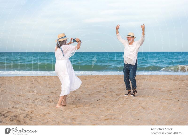 Woman shooting senior husband dancing on beach couple video fun dance seashore retire love smartphone together gadget memory moment content romantic using