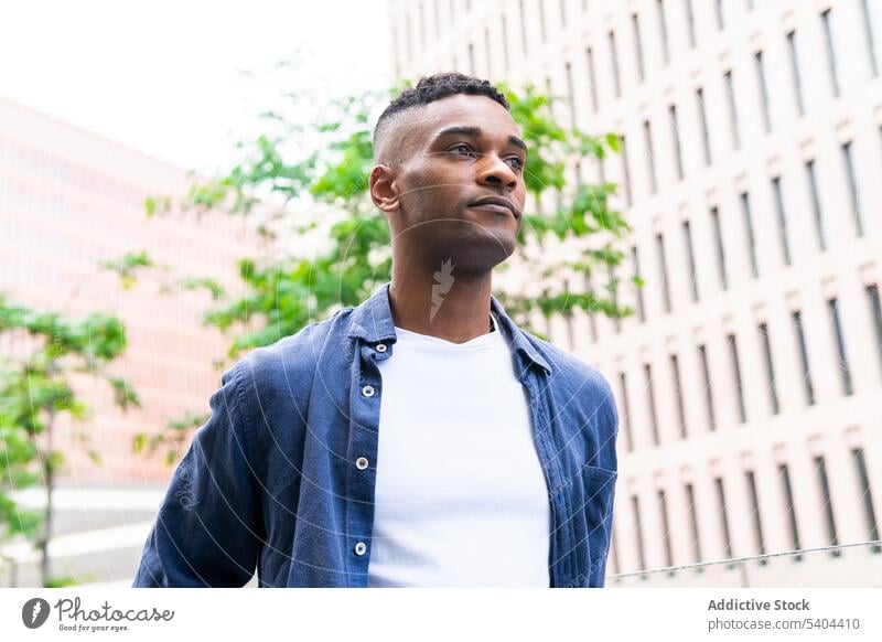 Black man walking while relaxing on day off cityscape green tree chill self confident male black african american weekend leisure pastime recreation street