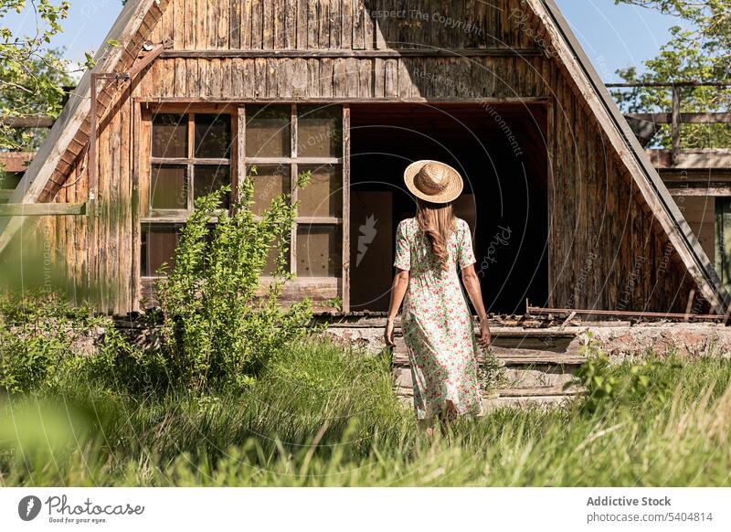 Anonymous woman walking to house in countryside summer shed barn village rural nature dress wooden bright land freedom building alone structure green