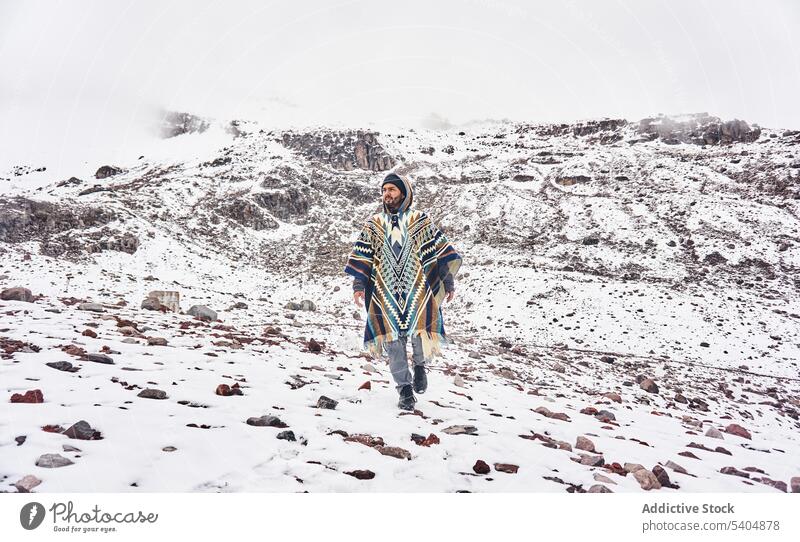 Young man walking on snowy terrain of mountain slope traveler wanderlust explore nature cold admire poncho male young vacation beard landscape adventure trip