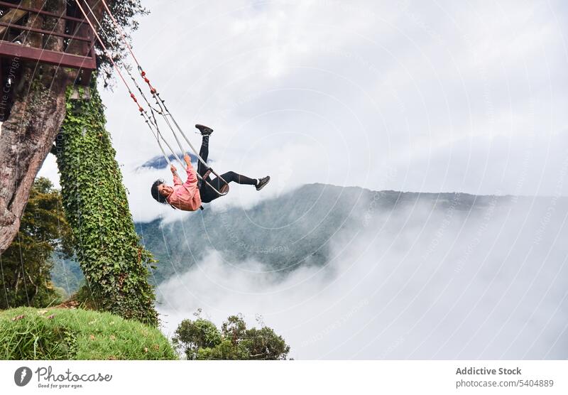 Happy young woman swinging on rope and enjoying amazing view of clouds and mountains smile summer cheerful adventure female happy nature cloudy freedom laugh