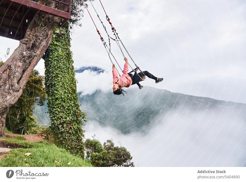 Happy young woman swinging on rope and enjoying amazing view of clouds and mountains smile summer cheerful adventure female happy nature cloudy freedom laugh