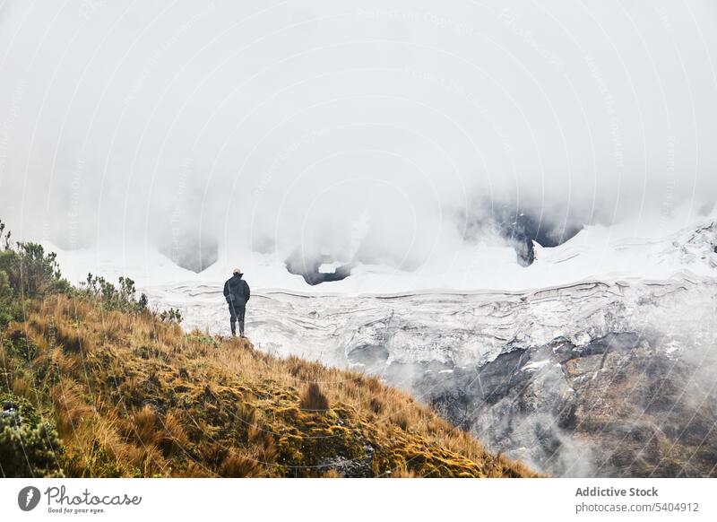 Unrecognizable traveler trekking on grassy slope by cloudy mountain hill admire volcano nature top snow landscape valley picturesque adventure altar countryside