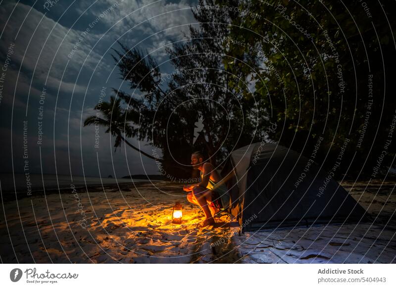 Man sitting near tent on sandy beach at sunset man night lamp evening twilight sea nature tree coast shore peaceful calm idyllic trip africa camp tranquil