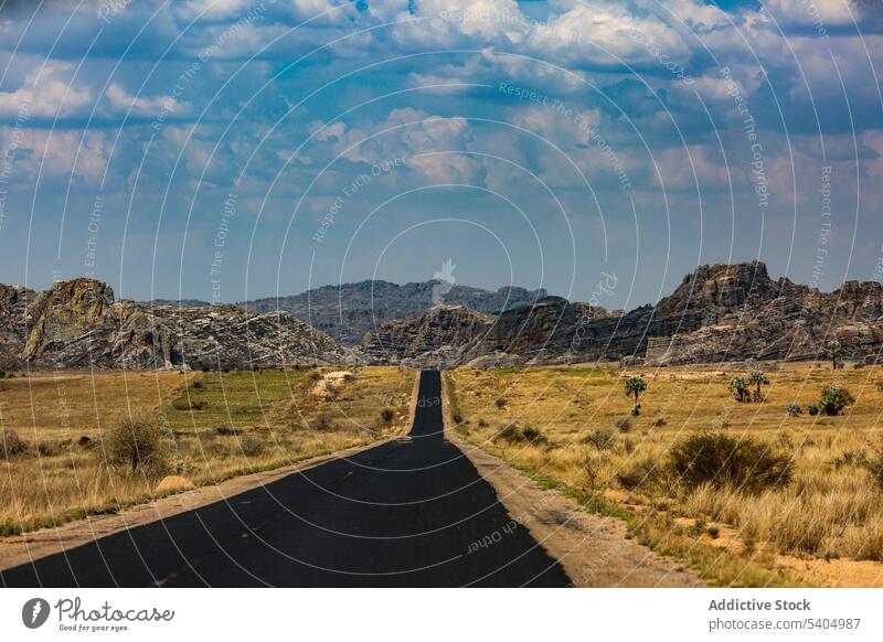 Empty asphalt road with mountains and dried grass countryside bush blue sky rocky landscape roadway empty tree daytime hill cloudy route daylight nature