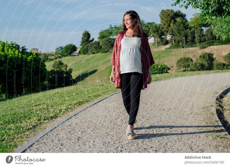 Happy pregnant woman walking in park expect belly baby bump maternal stroll green smile female pregnancy await childbearing prenatal anticipate motherhood mom