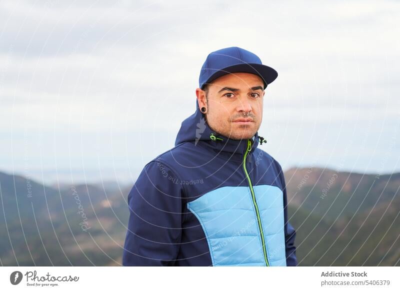 Confident traveler standing in mountains during hiking man hiker portrait serious el garbi trekking adventure nature highland cap jacket blue tourism journey