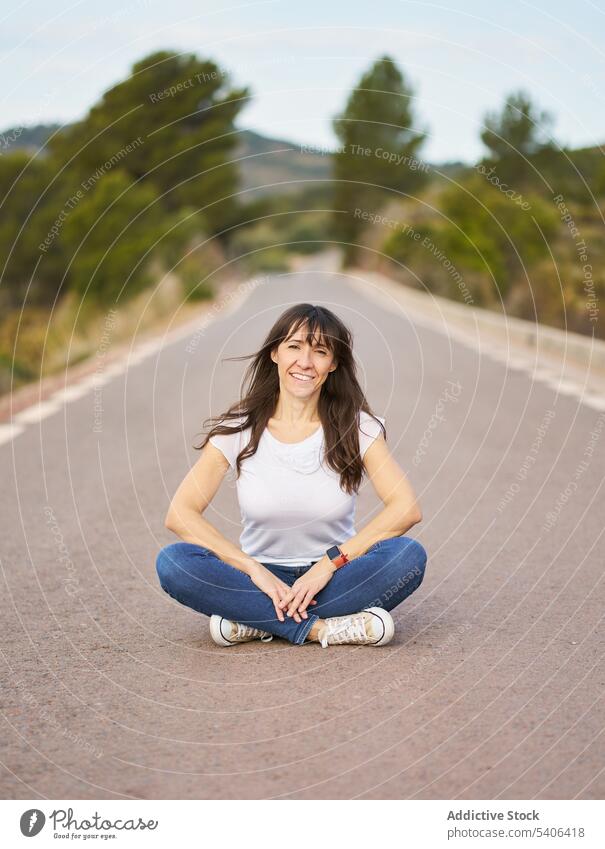 Delighted female tourist sitting on road woman traveler asphalt way trip smile route countryside tourism lady cheerful wanderlust path hispanic delight ethnic