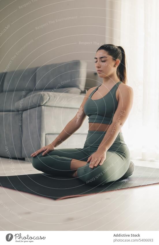 Beautiful young woman doing online yoga at home sportswoman lotus pose meditate padmasana mindfulness calm relax practice mat female slim wellness zen position