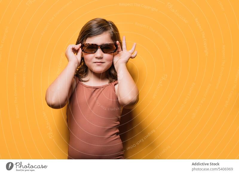 Cute little girl in swimsuit touching sunglasses and looking at camera style confident child summer holiday cool portrait serious model fashion kid swimwear