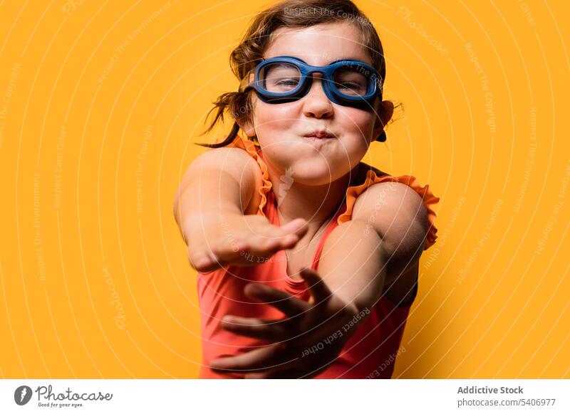 Joyful child pretending to be swimmer in yellow studio girl puff out cheeks funny imitate vacation activity positive portrait swimwear cheerful kid goggles