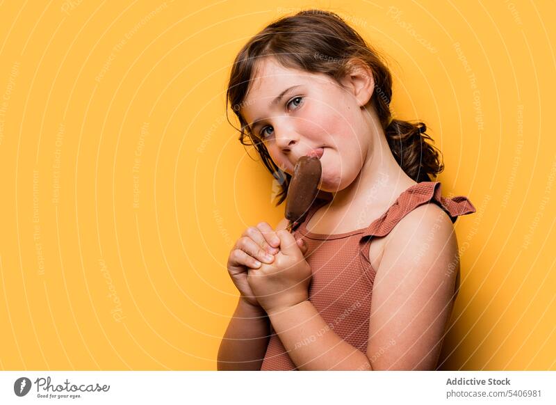 Hungry cute kid eating ice cream in yellow studio child lick chocolate sweet delicious summer vacation portrait girl dessert childhood swimsuit brunette