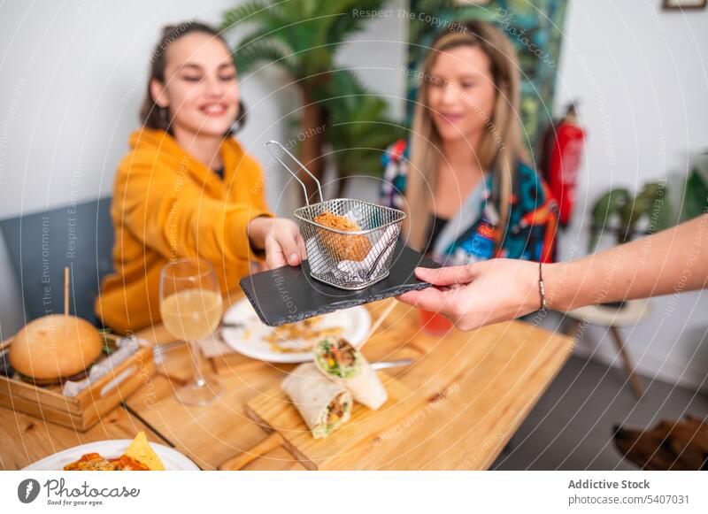 Smiling friends having fun while eating snacks and fries women fried food dish tasty various basket table friendship dinner cafe female smile drink roast