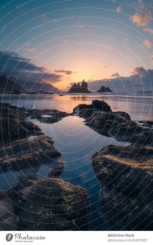 Rocky coast of sea under cloudy sky at sunset with distant mountains shore rock silhouette landscape calm sundown evening scenic picturesque scenery twilight