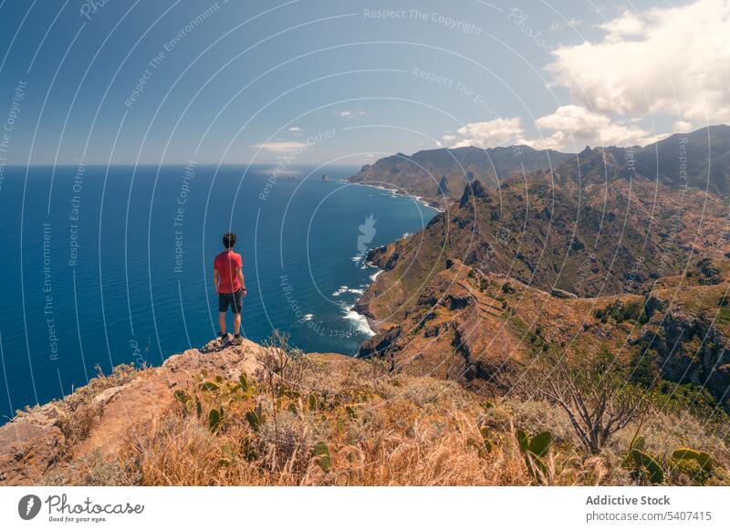 Young man in casual clothes standing on cliff admiring seascape mountain traveler hiker nature landscape adventure male trip tourism vacation tenerife spain