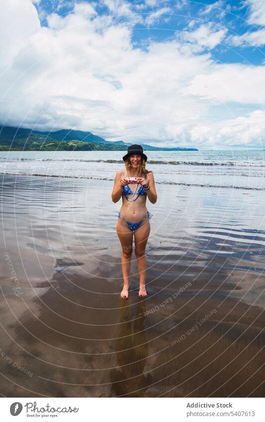 Smiling woman standing on seashore with retro camera resort film photo camera beach summer wave smile cheerful female young uvita puntarenas costa rica america