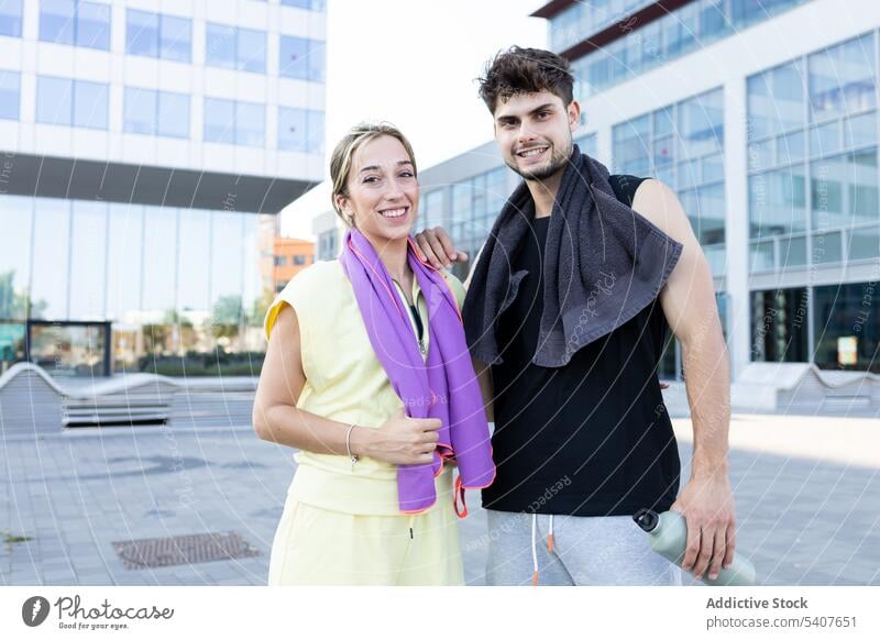 Happy young couple standing on city street in daylight near glass walled building towel bottle hydrate smile relationship love close positive happy athlete