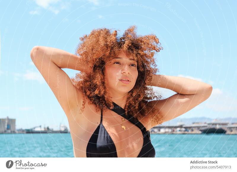 Carefree ethnic woman against blue sky enjoy summer sun carefree bikini top content relax afro female hairstyle vacation slim shorts cheerful sunny holiday