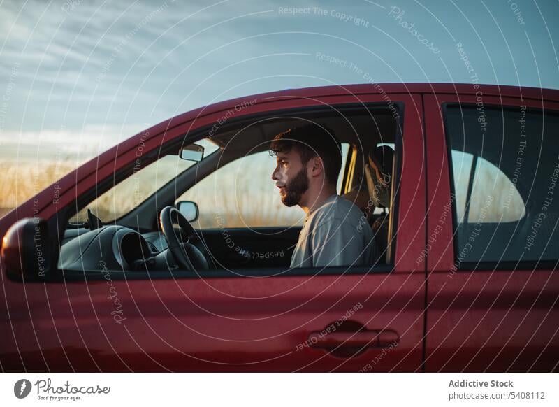 Bearded young man sitting in car in nature drive parked roadside vehicle transport automobile countryside road trip journey male travel casual white shirt beard