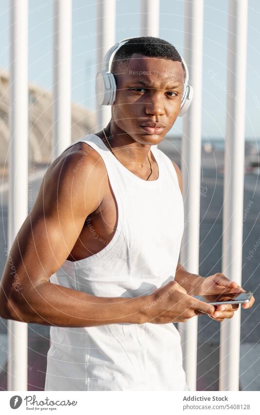 Black serious sportive man using smartphone during workout runner browsing headphones listen training athlete break sportsman internet surfing gadget sportswear