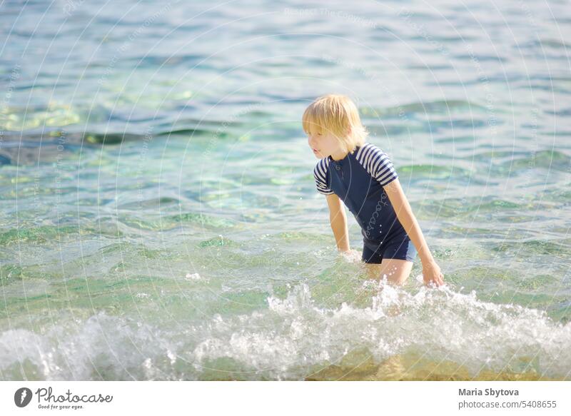 Cute preteen boy is bathing in a sea. Fun beach holiday for children. Summer vacation for kids. UV protection swimwear clothes sun play fun family water