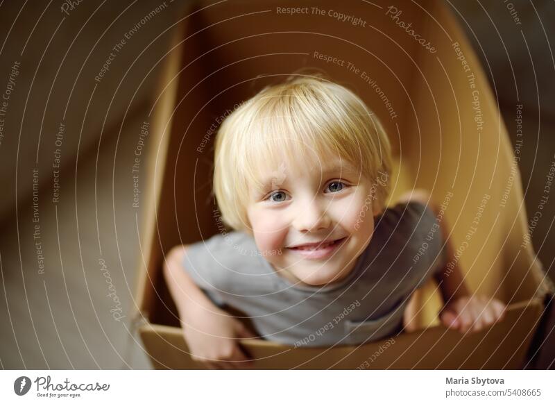 Cute preschool boy playing in a cardboard box during family's move to a new home. Kids play is a way of development of creative abilities. child kid imagination