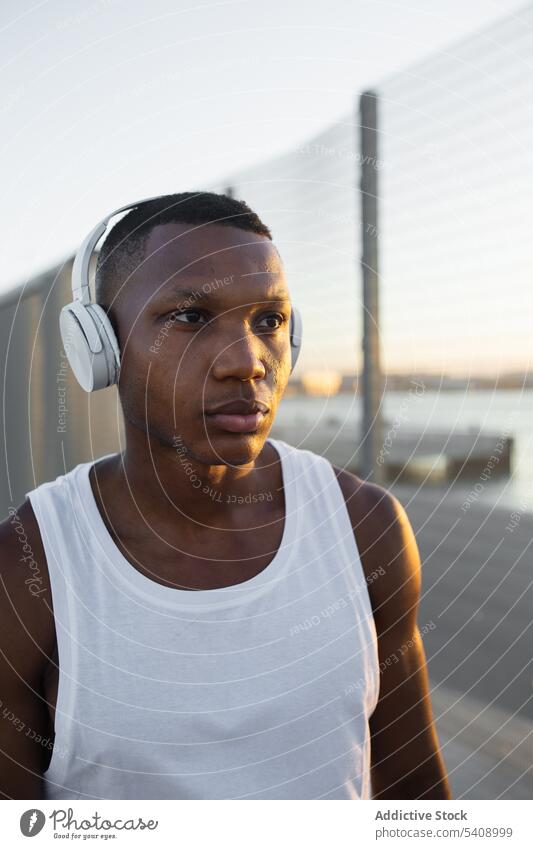 Black sportsman in headphones resting after training athlete serious muscular sporty music listen fit male sportswear lifestyle wellbeing device activity