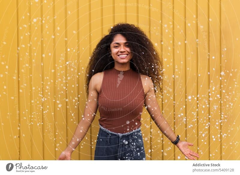 Black woman scattering confetti on street toss having fun cheerful delight festive celebrate event female ethnic black african american city happy joy smile