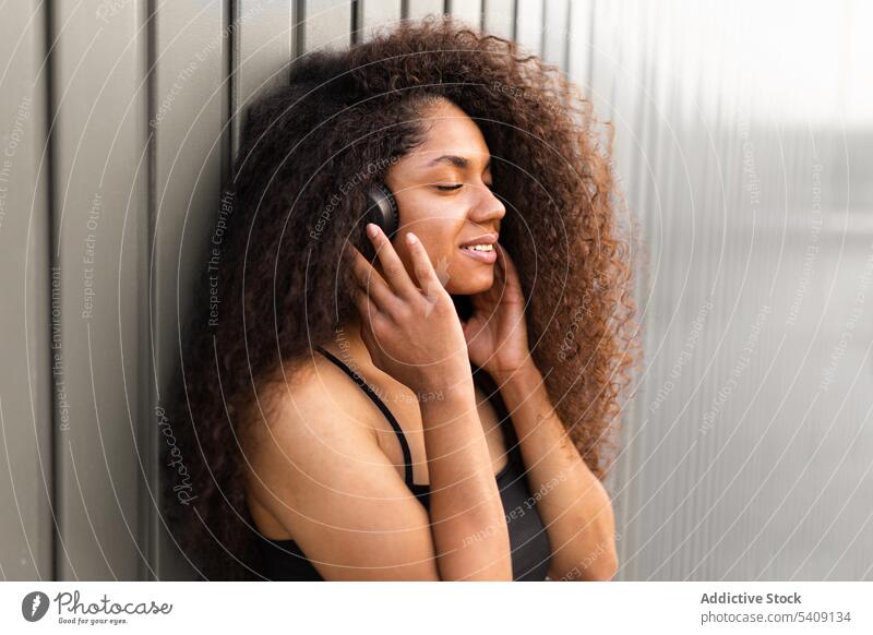 Charming ethnic woman with headphones on street curly hair afro hairstyle charming smile natural beauty female listen black african american city trendy rest