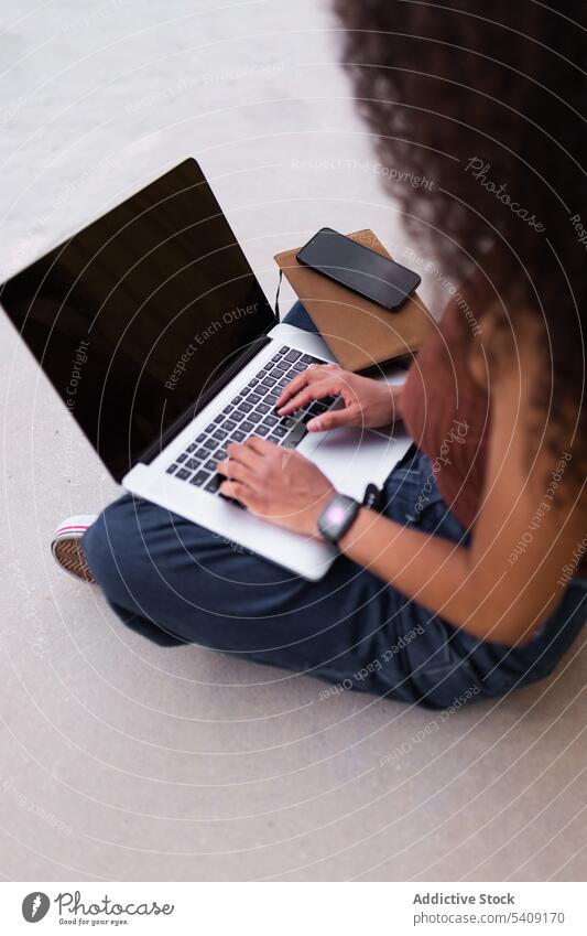 Cheerful African American self employed woman sitting on street with laptop smartphone selfie self portrait freelance curly hair city entrepreneur female ethnic