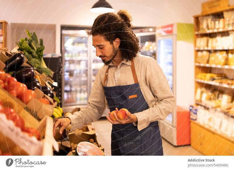 Ethnic male seller choosing peaches during work in supermarket man grocery fruit select counter fresh food healthy food vegetable positive young hispanic ethnic