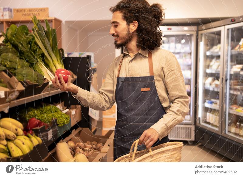 Smiling ethnic worker choosing assorted veggies during work in grocery store man bell pepper vegetable smile choose supermarket product healthy food fresh male