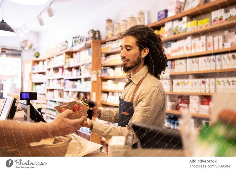 Young ethnic male cashier scanning products during work in eco friendly store man strawberry seller fruit supermarket fresh food customer ripe young hispanic