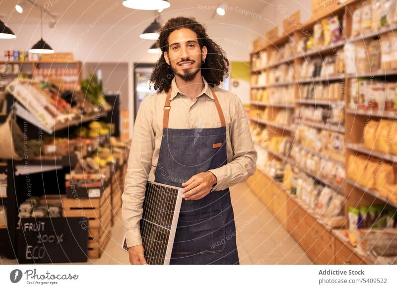 Cheerful ethnic seller holding portable solar panel in store man supermarket shop happy cheerful worker positive purchase modern device shopper energy smile